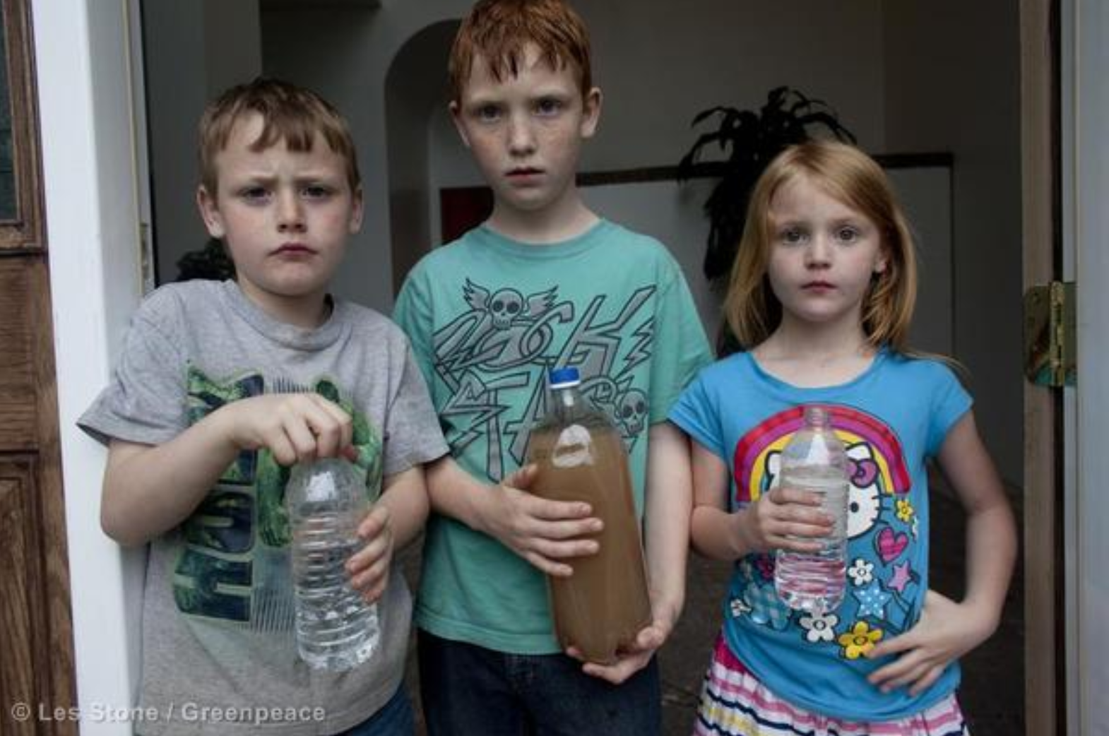 Jessica, Justin, and Joshua Ely hold bottles of water at their house in Dimock. The one at center is contaminated water from their tap.